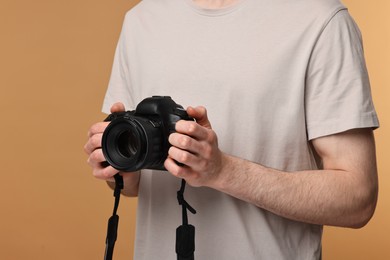 Photo of Photographer holding camera on beige background, closeup