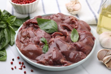 Photo of Plate of raw chicken liver with basil on white table, closeup