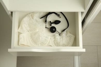 Photo of Anal plug, ball gag and women's underwear in open drawer of nightstand indoors, above view. Sex toys