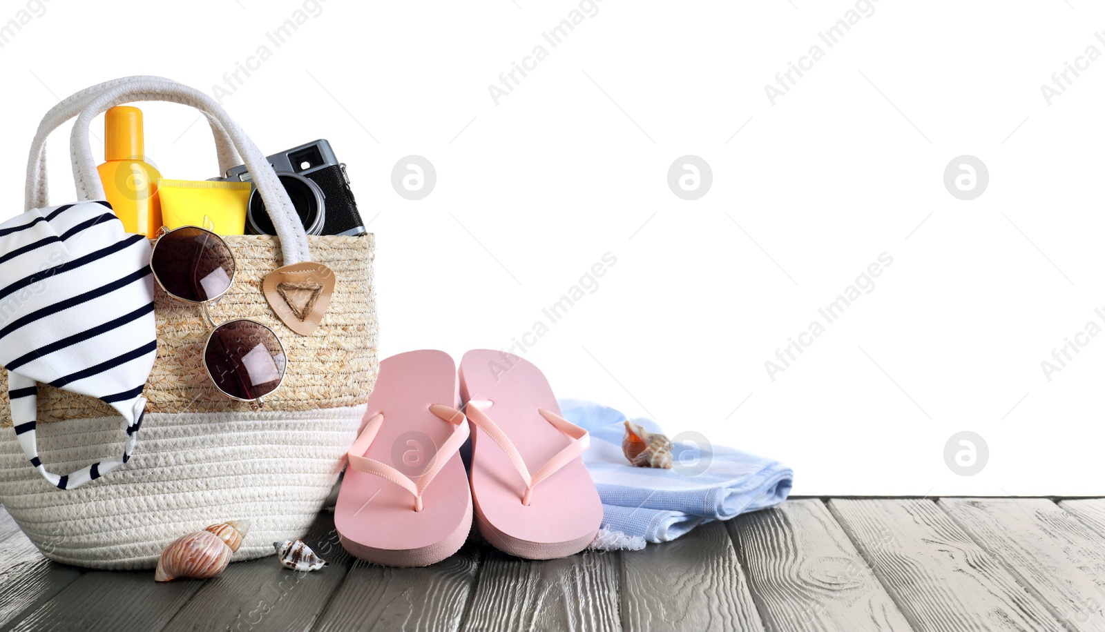 Photo of Bag with different beach objects on grey wooden table against white background