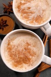 Cups of delicious eggnog with anise and cinnamon on grey table, flat lay