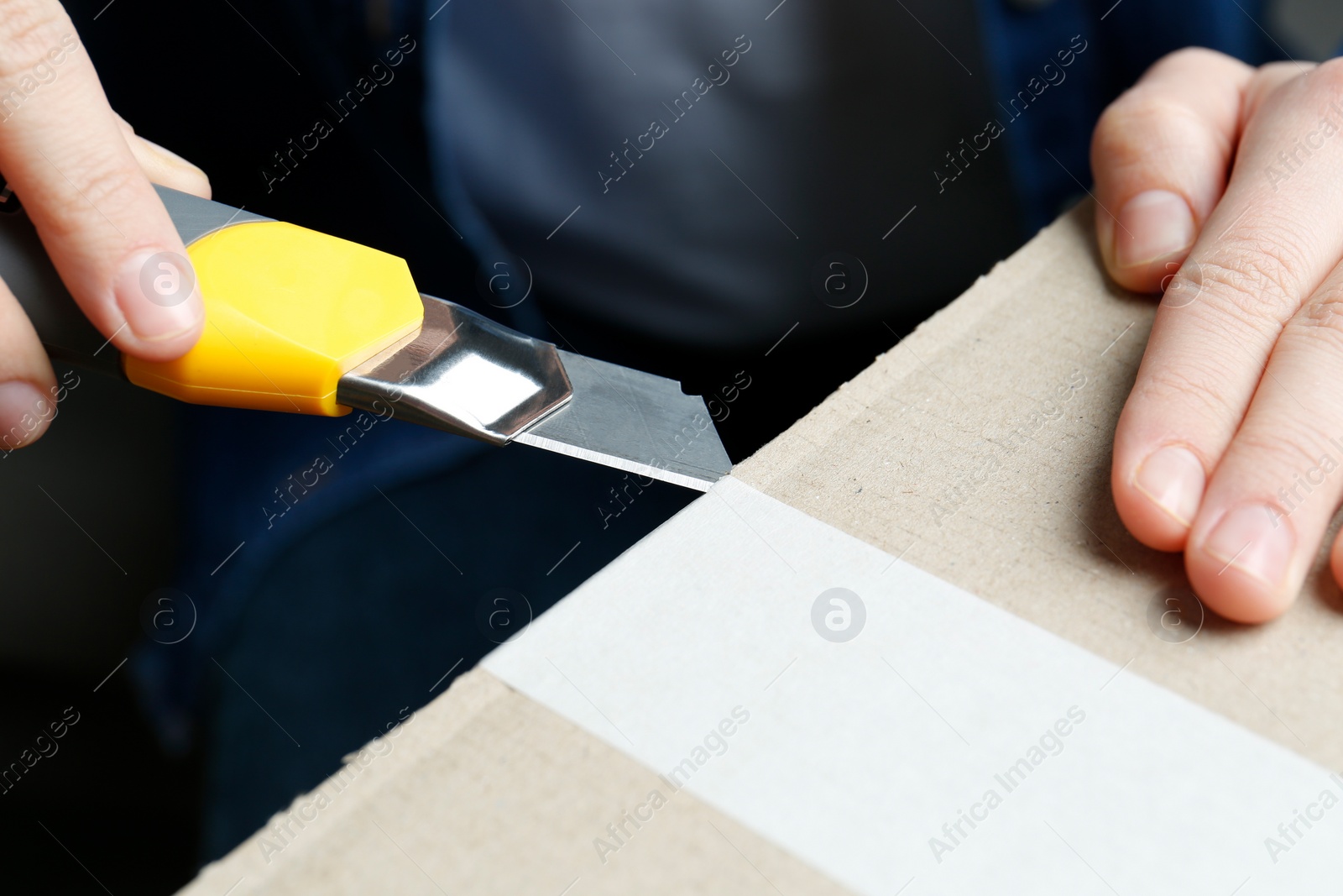 Photo of Man using utility knife to open parcel, closeup