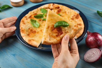 Photo of Woman taking piece of delicious khachapuri with cheese and basil at light blue wooden table, closeup
