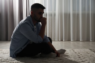 Photo of Sad man sitting on floor near window. Space for text