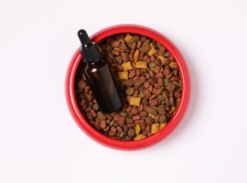 Glass bottle of tincture and dry pet food in bowl on white background, top view