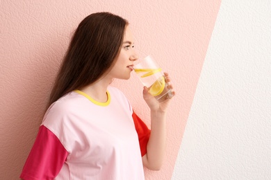 Young woman drinking lemon water on color background