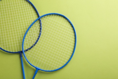 Badminton rackets on light green background, flat lay. Space for text