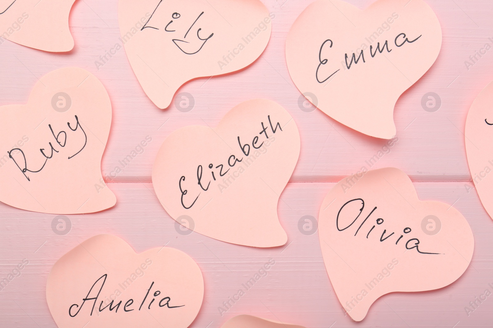 Photo of Paper stickers with different names on pink wooden background, flat lay. Choosing baby's name