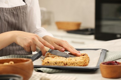 Photo of Woman cutting granola bars at table in kitchen, closeup