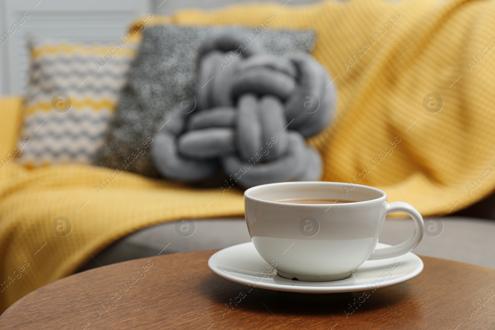 Photo of Cup of hot drink on table near sofa with pillows in living room