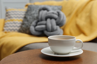 Cup of hot drink on table near sofa with pillows in living room