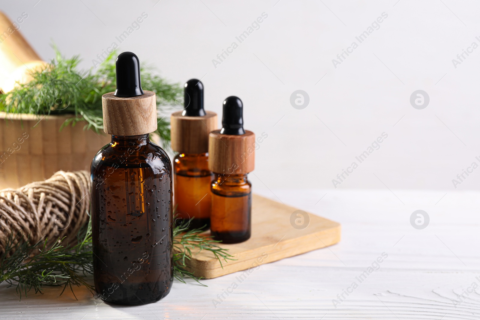 Photo of Bottles of essential oil and fresh dill on white wooden table, closeup. Space for text