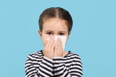 Photo of Girl blowing nose in tissue on light blue background. Cold symptoms