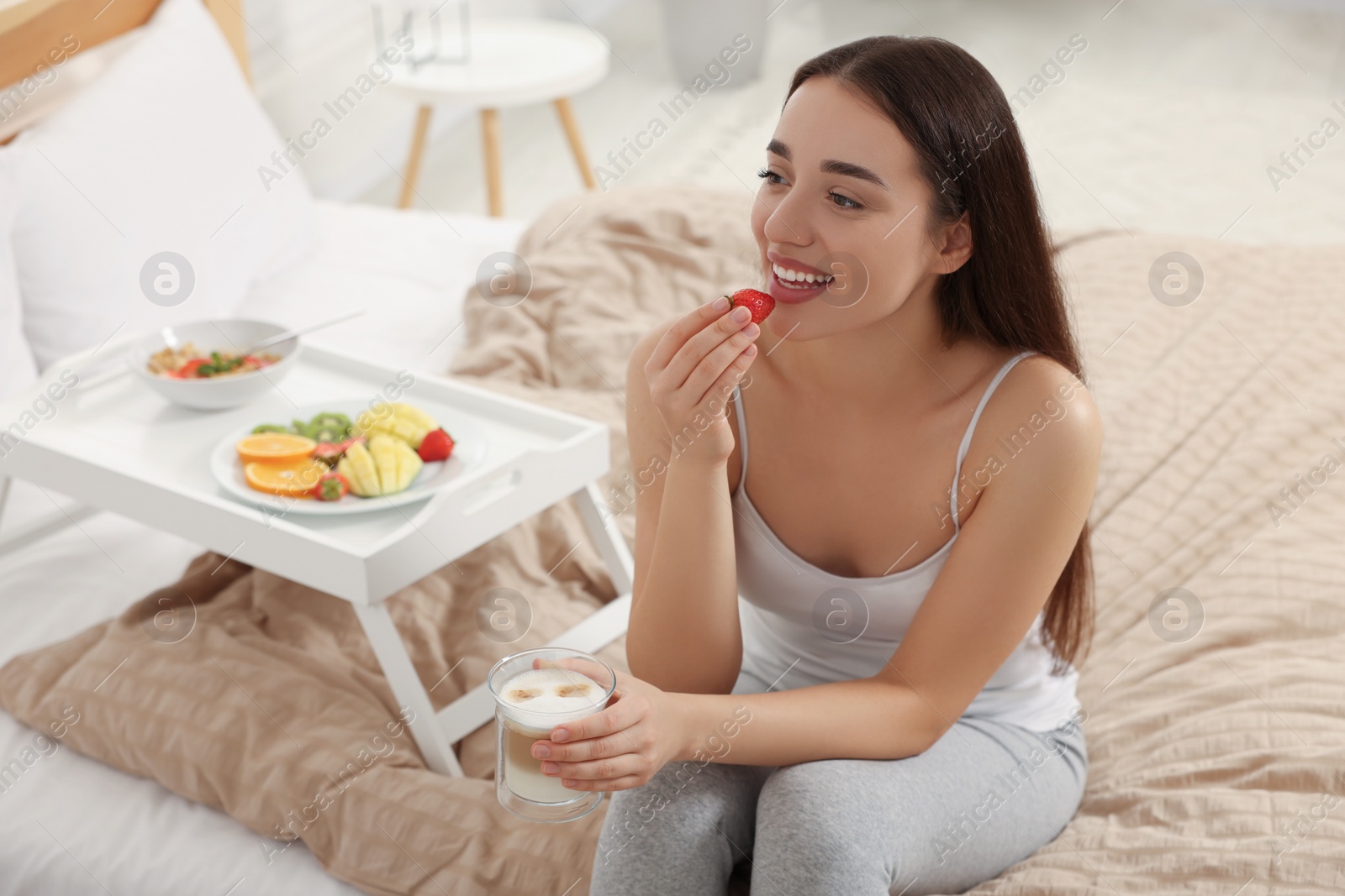 Photo of Happy young woman having breakfast near white tray on bed at home