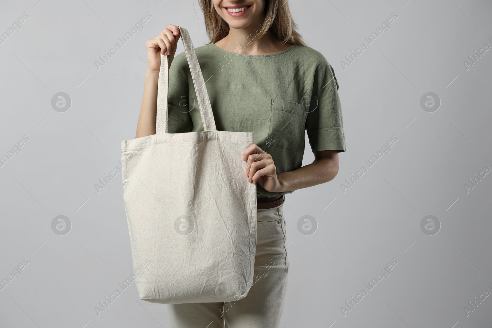 Photo of Happy young woman with blank eco friendly bag on light background, closeup