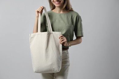 Happy young woman with blank eco friendly bag on light background, closeup