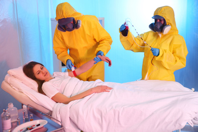Paramedics wearing protective suits examining patient with virus in quarantine ward