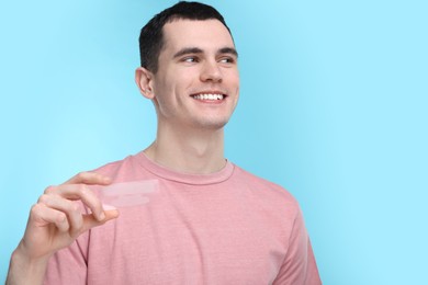 Photo of Young man with whitening strips on light blue background. Space for text