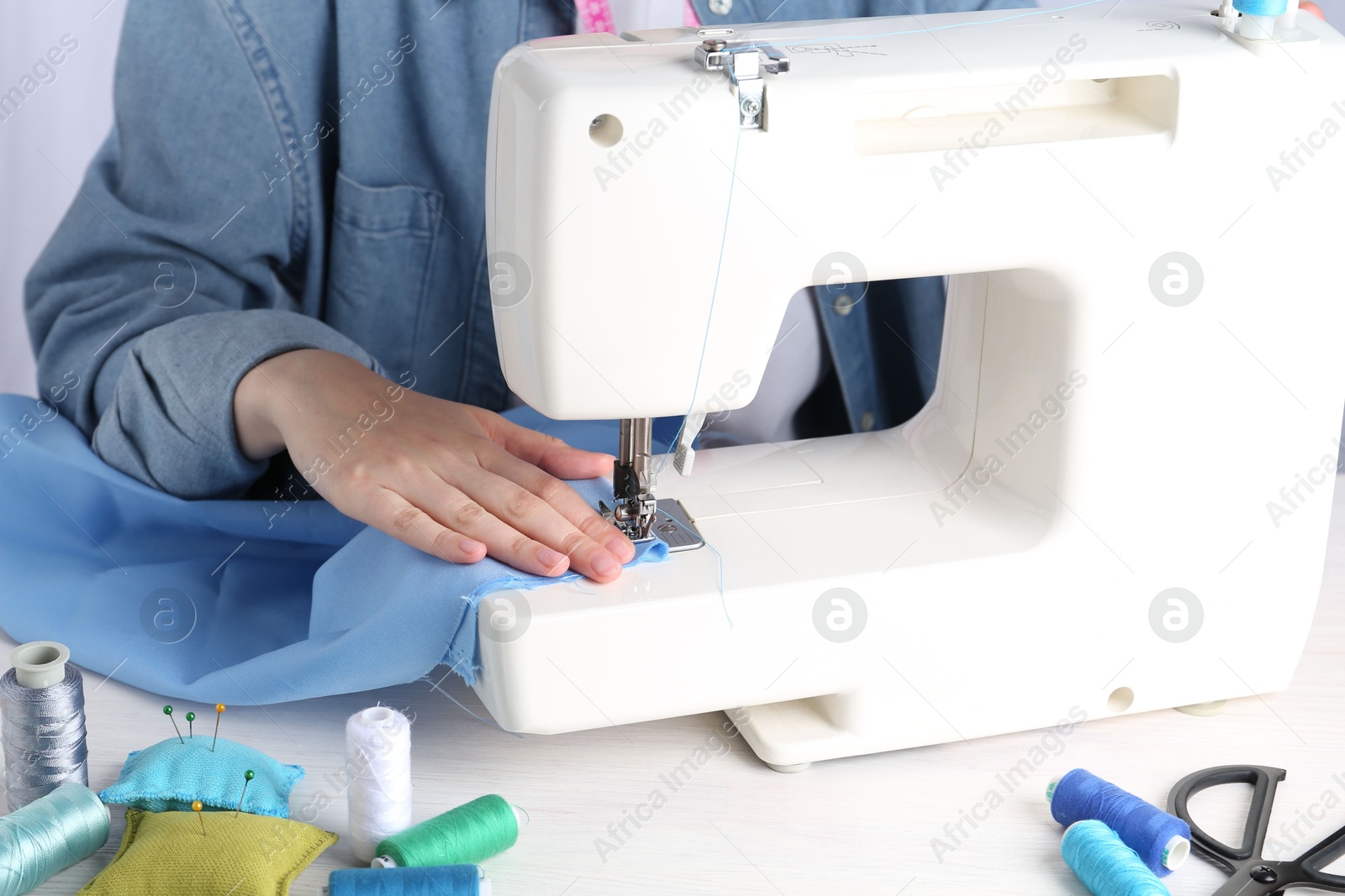 Photo of Seamstress working with sewing machine at white wooden table indoors, closeup