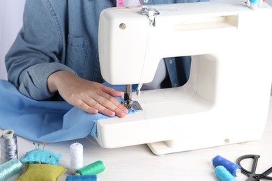 Photo of Seamstress working with sewing machine at white wooden table indoors, closeup