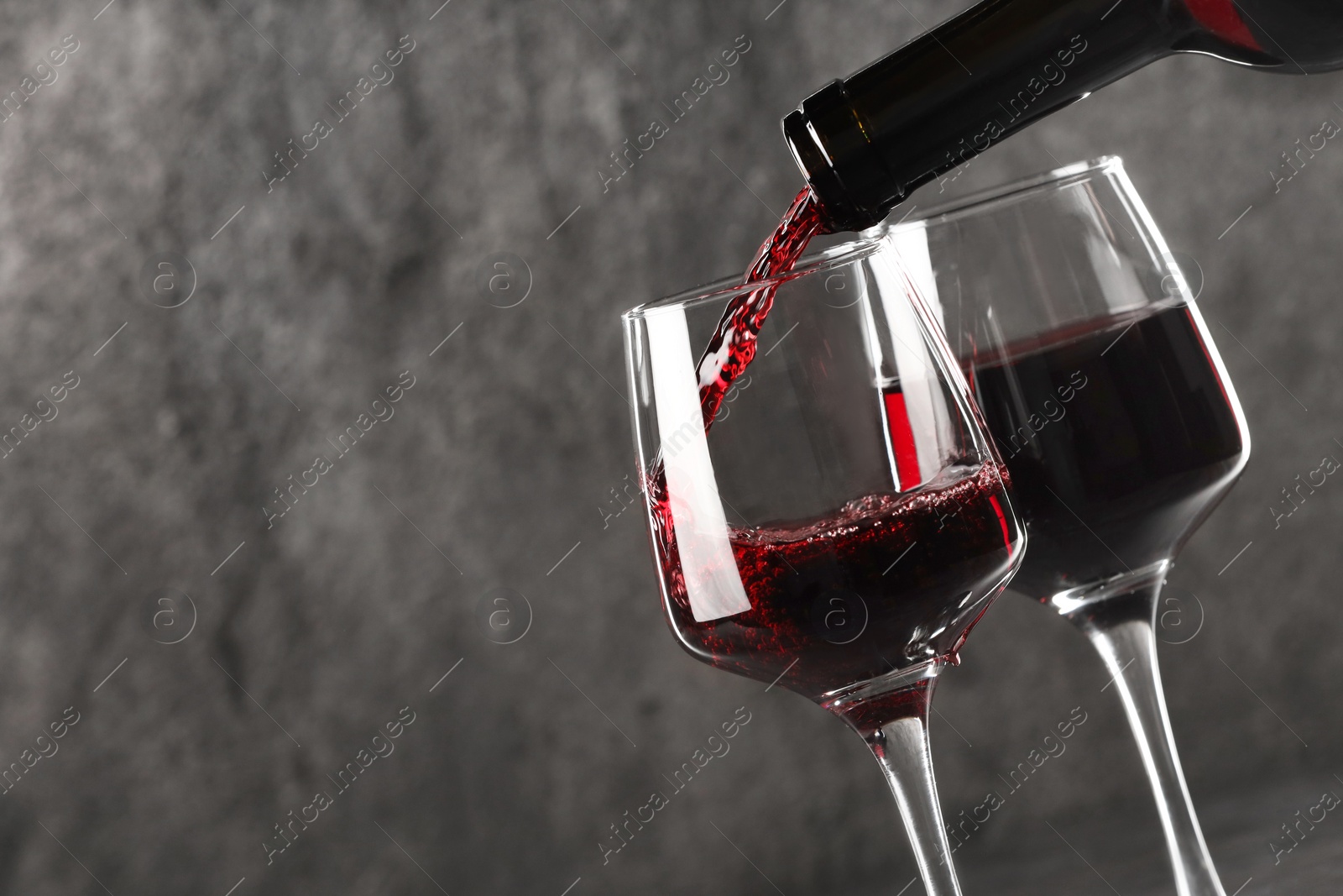 Photo of Pouring red wine into glass against grey background, closeup. Space for text