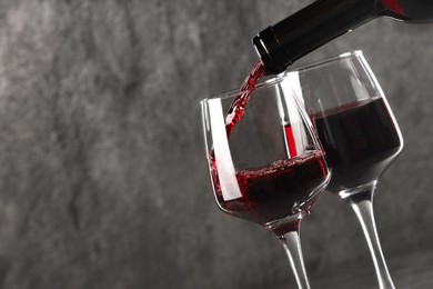 Photo of Pouring red wine into glass against grey background, closeup. Space for text