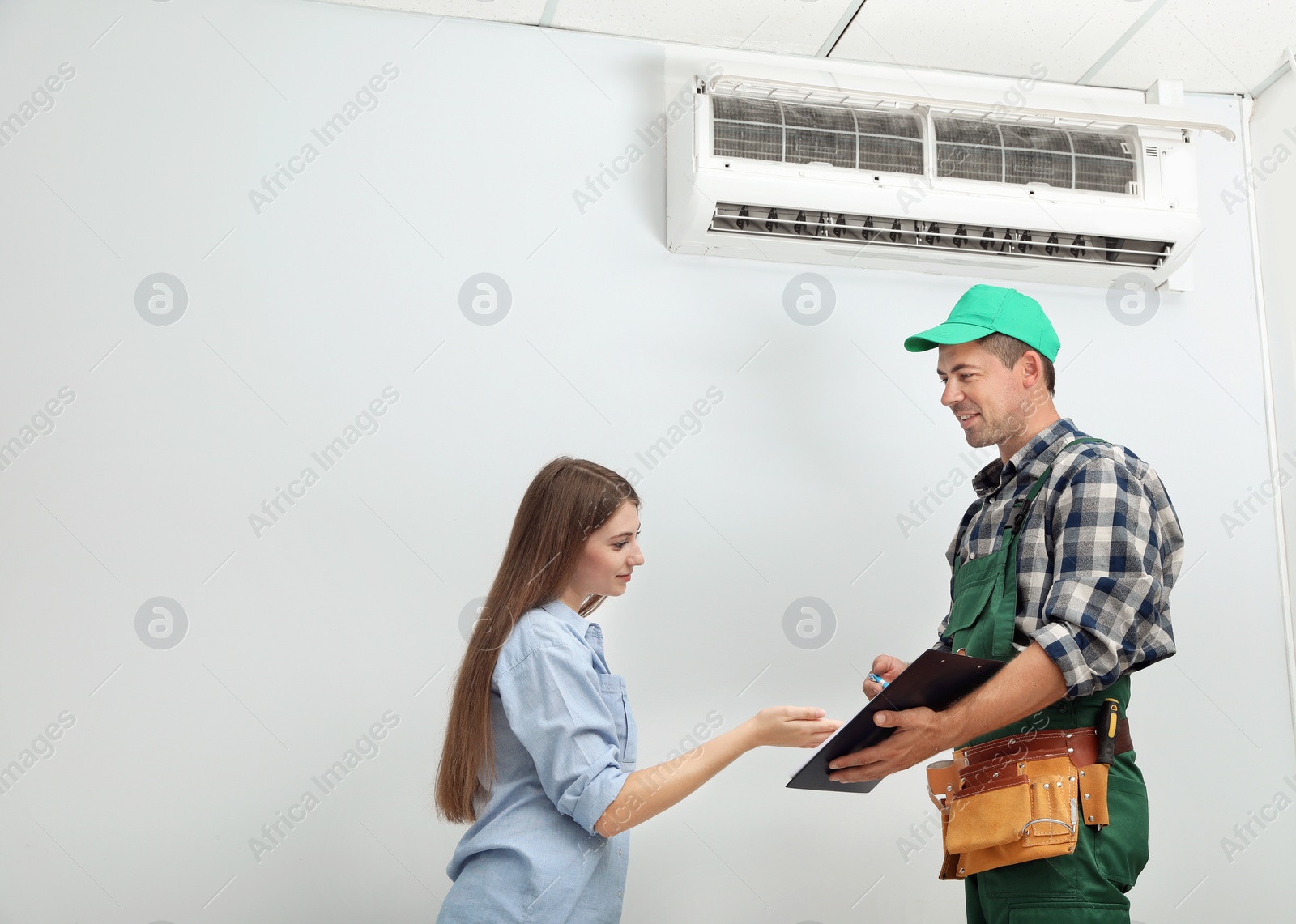 Photo of Male technician speaking with woman about air conditioner indoors