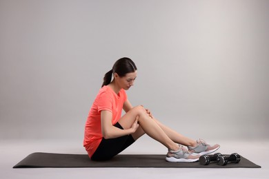 Young woman suffering from leg pain on exercise mat against grey background