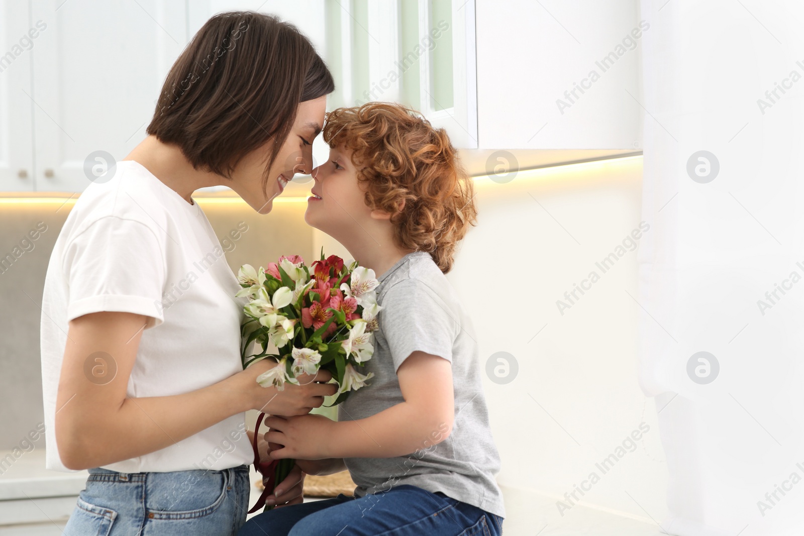 Photo of Happy woman with her cute son and bouquet of beautiful flowers in kitchen, space for text. Mother's day celebration