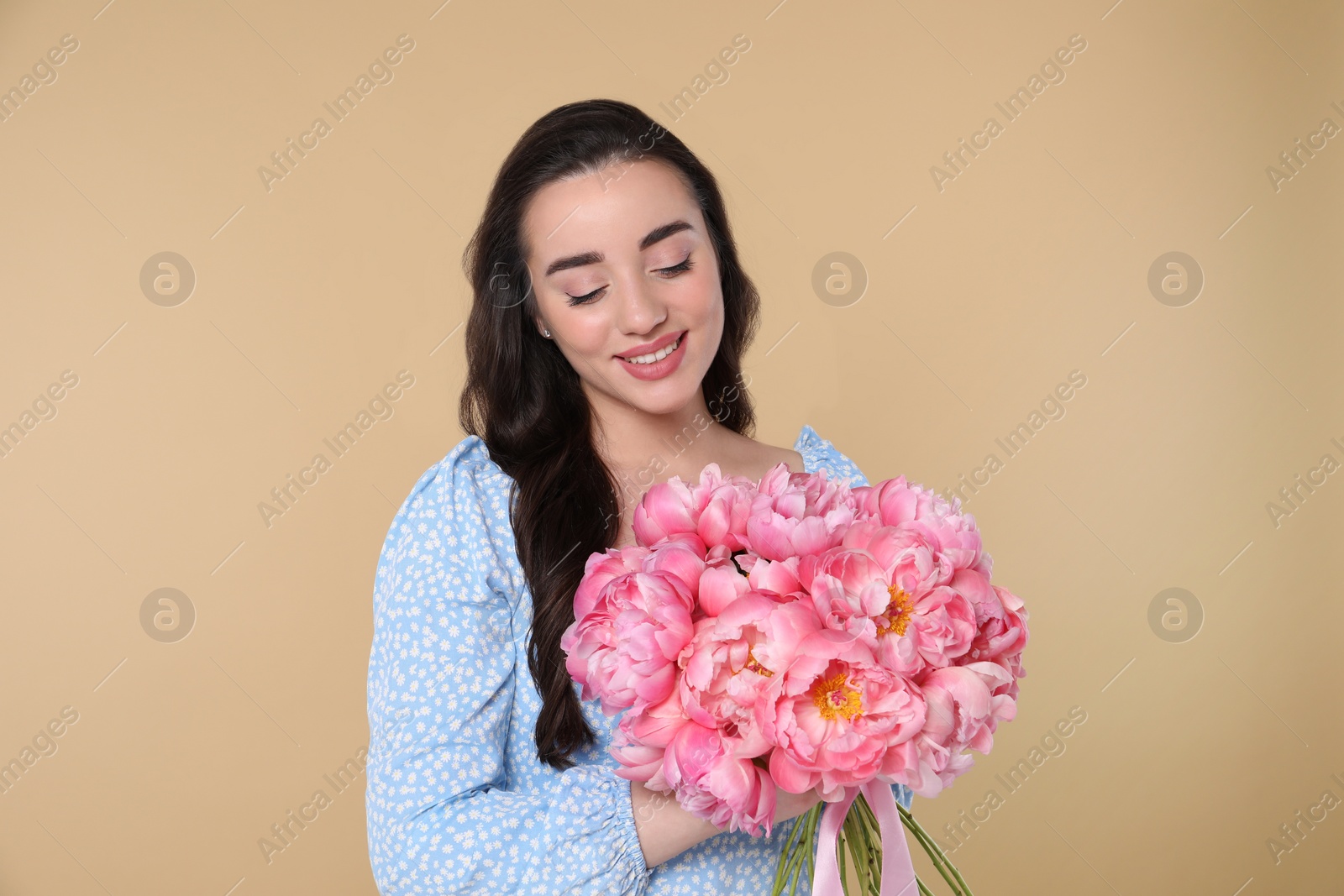 Photo of Beautiful young woman with bouquet of pink peonies on beige background