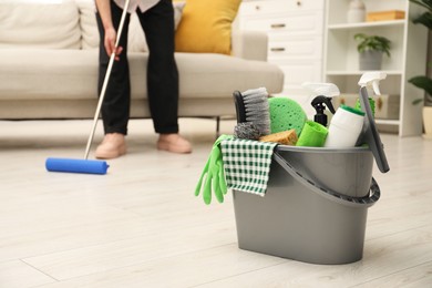 Photo of Woman cleaning floor, focus on different supplies in bucket at home