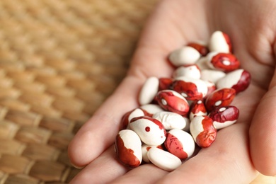 Photo of Woman holding pile of beans over wicker table, closeup. Vegetable seeds planting