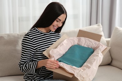 Happy woman opening parcel on sofa at home. Internet shopping