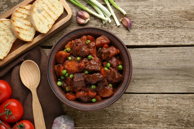 Photo of Delicious beef stew and ingredients on wooden table, flat lay. Space for text