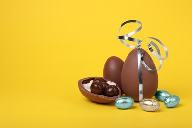 Photo of Delicious chocolate eggs and candies on yellow background. Space for text