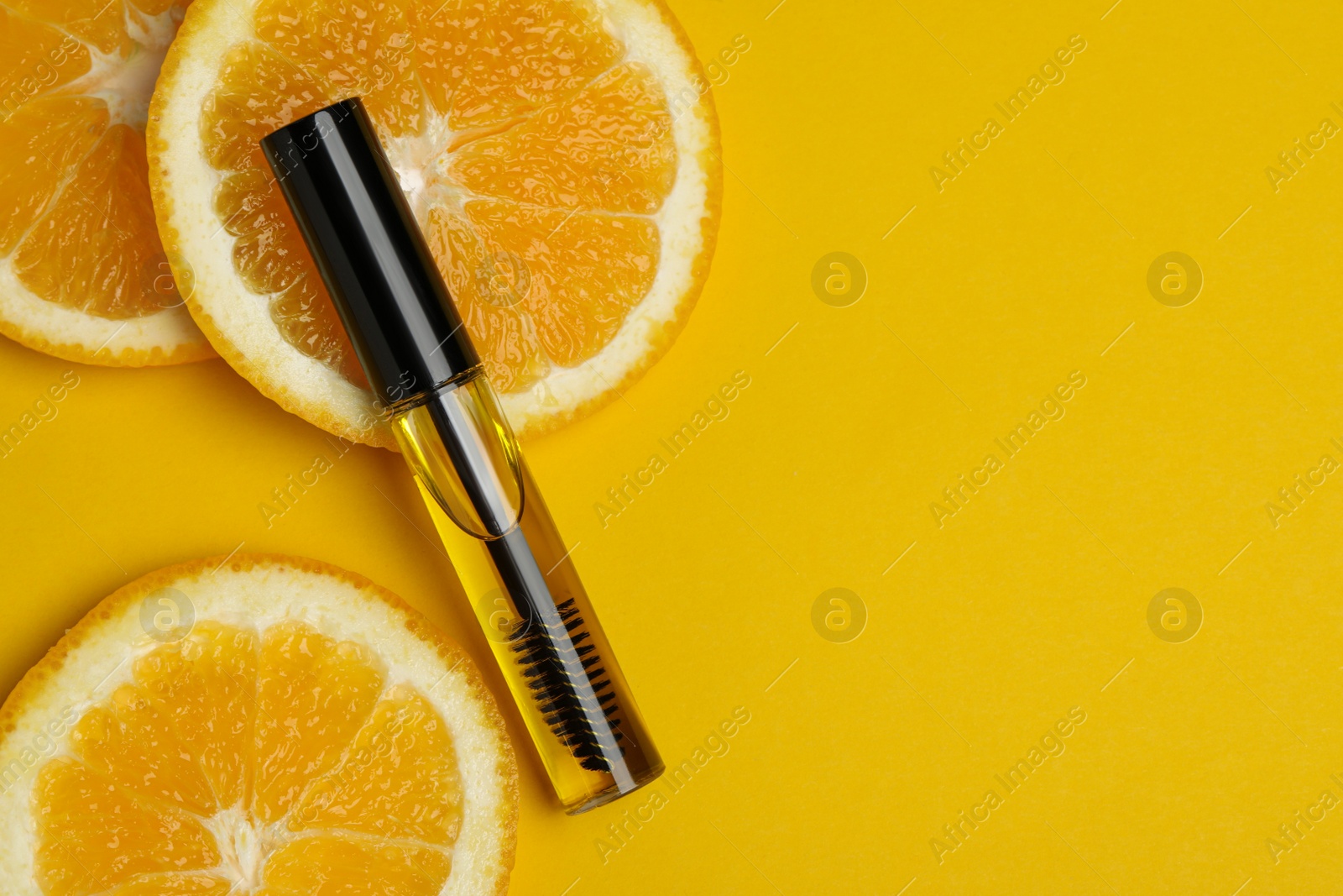 Photo of Tube of eyelash oil with fresh orange slices on yellow background, flat lay. Space for text