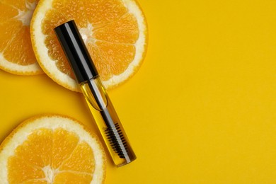 Tube of eyelash oil with fresh orange slices on yellow background, flat lay. Space for text