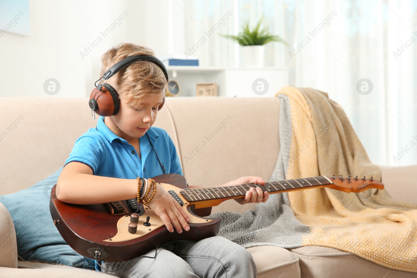 Photo of Cute little boy with headphones playing guitar on sofa in room. Space for text