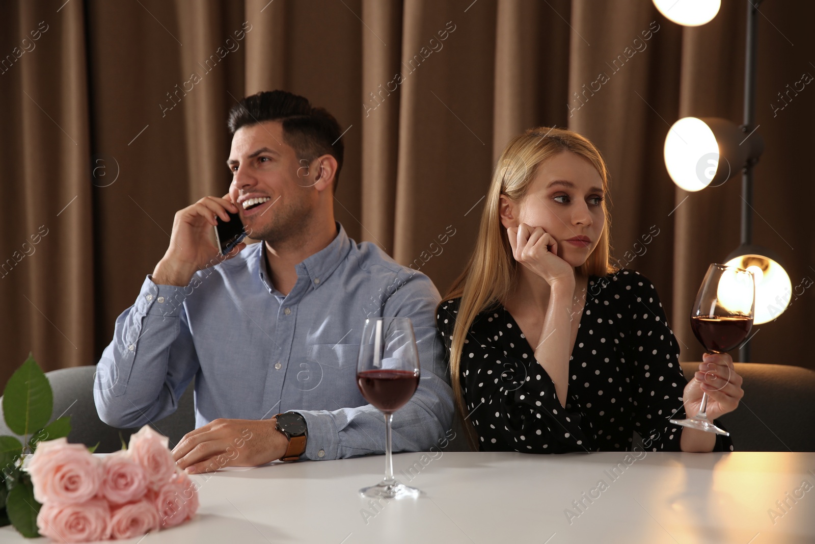 Photo of Man talking on phone instead of spending time with young woman during first date in restaurant