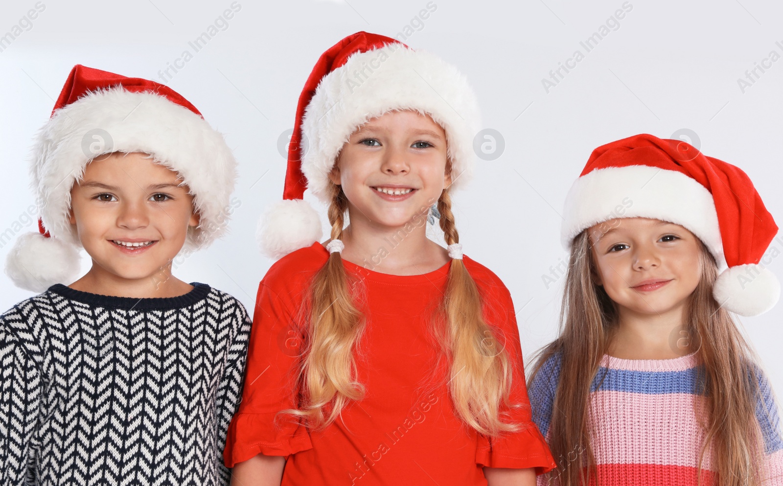 Photo of Happy little children in Santa hats on light grey background. Christmas celebration