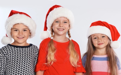 Happy little children in Santa hats on light grey background. Christmas celebration