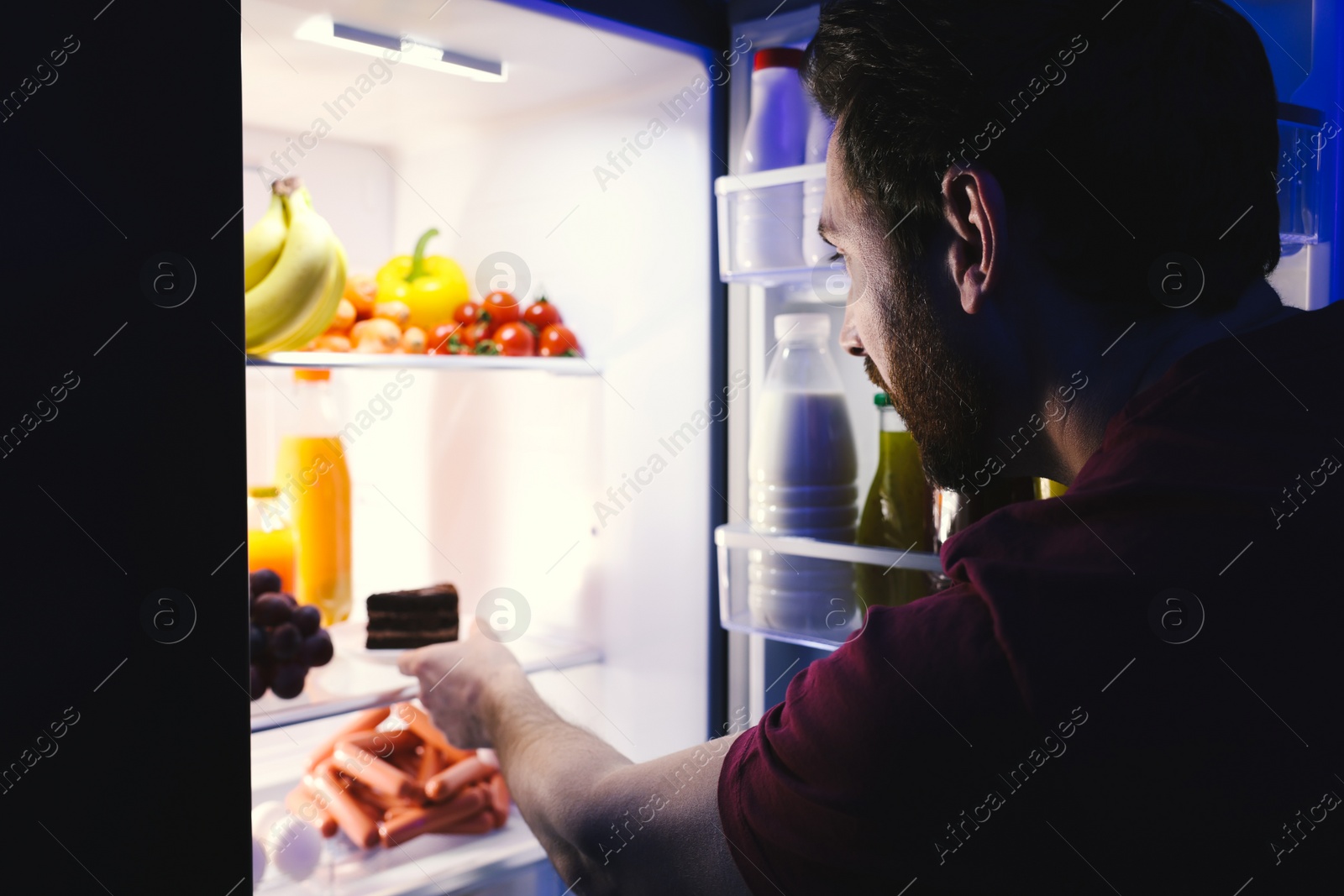 Photo of Man taking plate with cake from refrigerator in kitchen at night. Bad habit