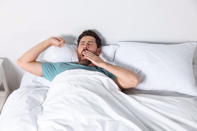 Photo of Handsome man yawning while lying on pillow in bed at home