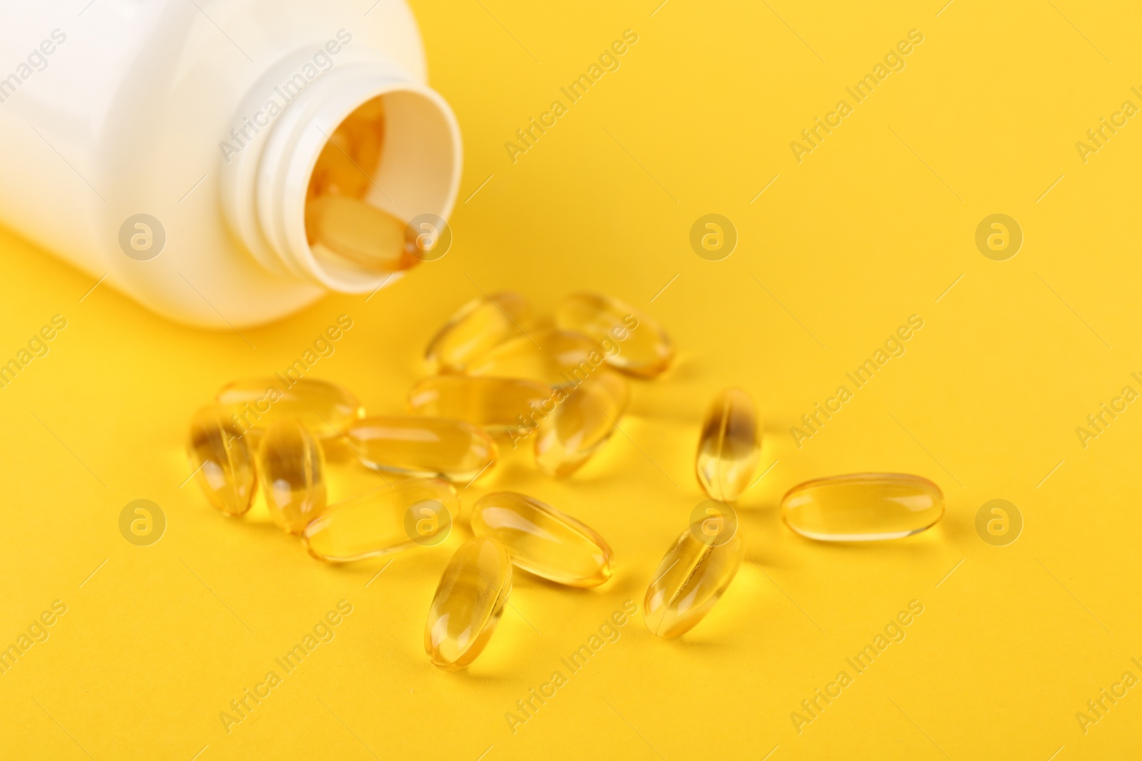 Photo of Vitamin capsules and medical bottle on yellow background, closeup