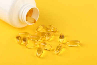 Photo of Vitamin capsules and medical bottle on yellow background, closeup