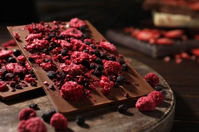 Photo of Chocolate bars with different freeze dried fruits on wooden board, closeup