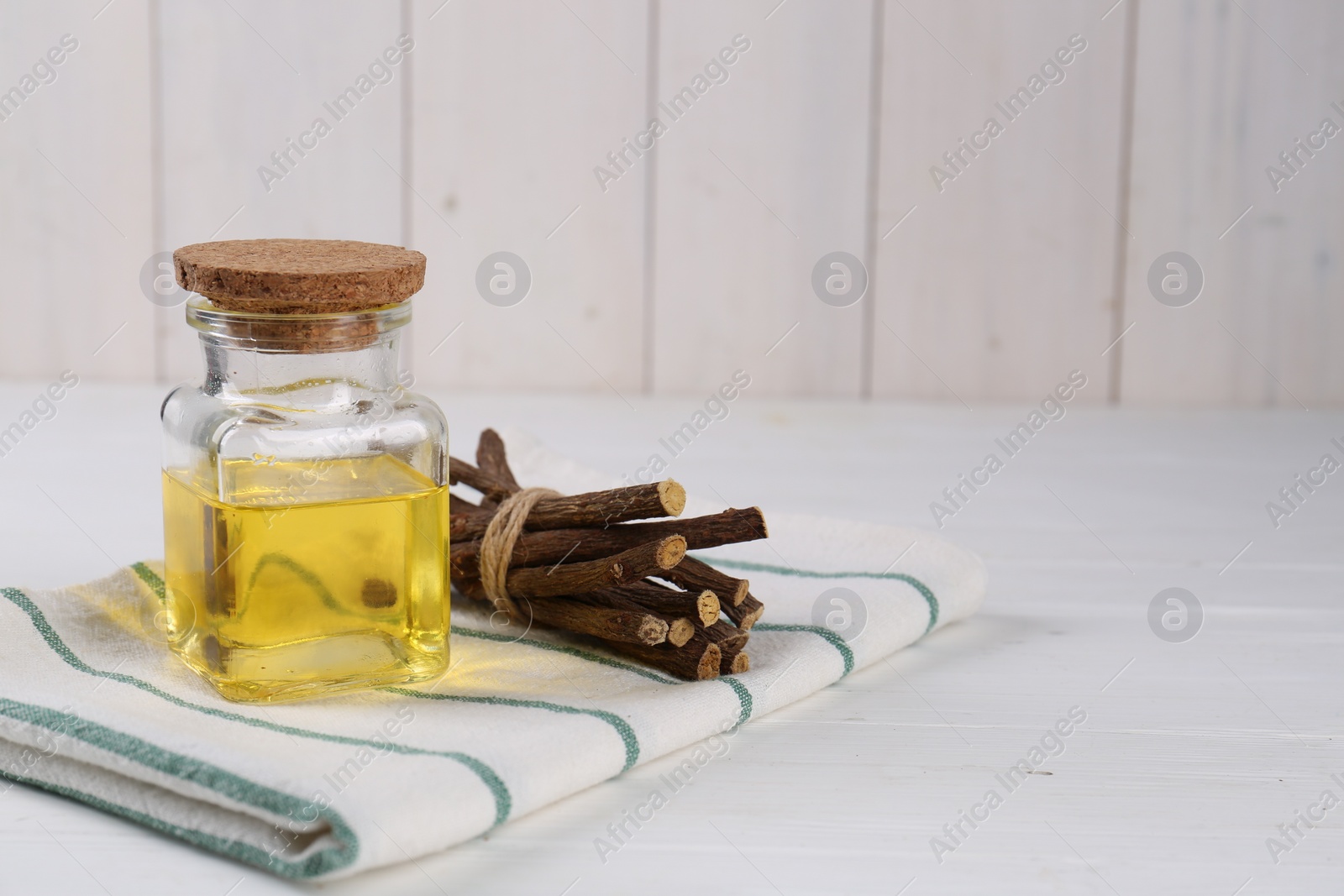 Photo of Dried sticks of licorice roots and essential oil on white wooden table. Space for text