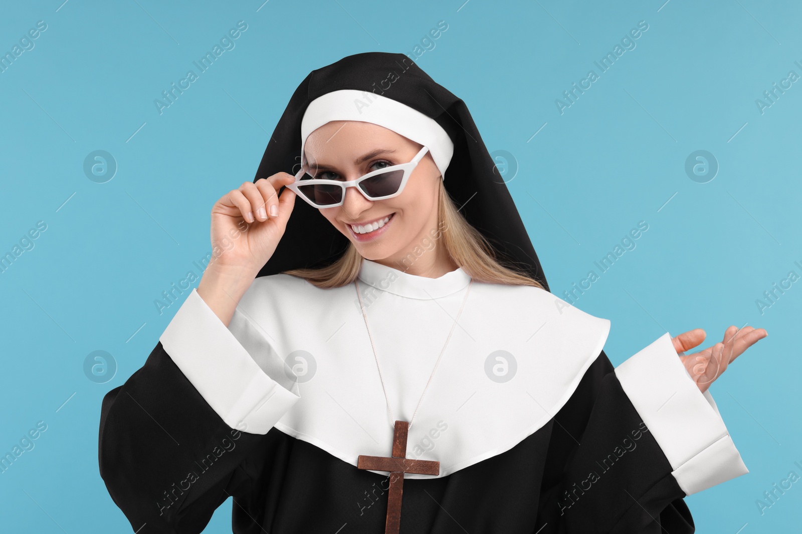 Photo of Happy woman in nun habit and sunglasses against light blue background