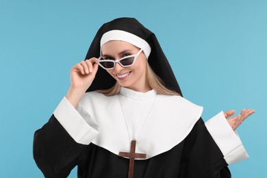 Happy woman in nun habit and sunglasses against light blue background