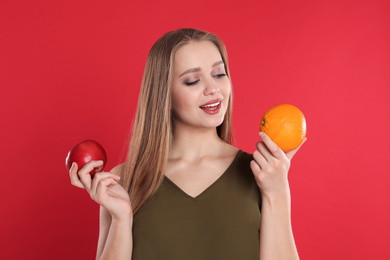 Photo of Young woman with apple and orange on red background. Vitamin rich food